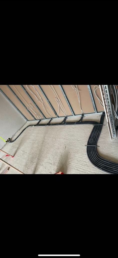 Kable elektryczne ułożone w korytkach na ścianie i suficie w surowym stanie, widoczne elementy konstrukcyjne sufitu podwieszanego.