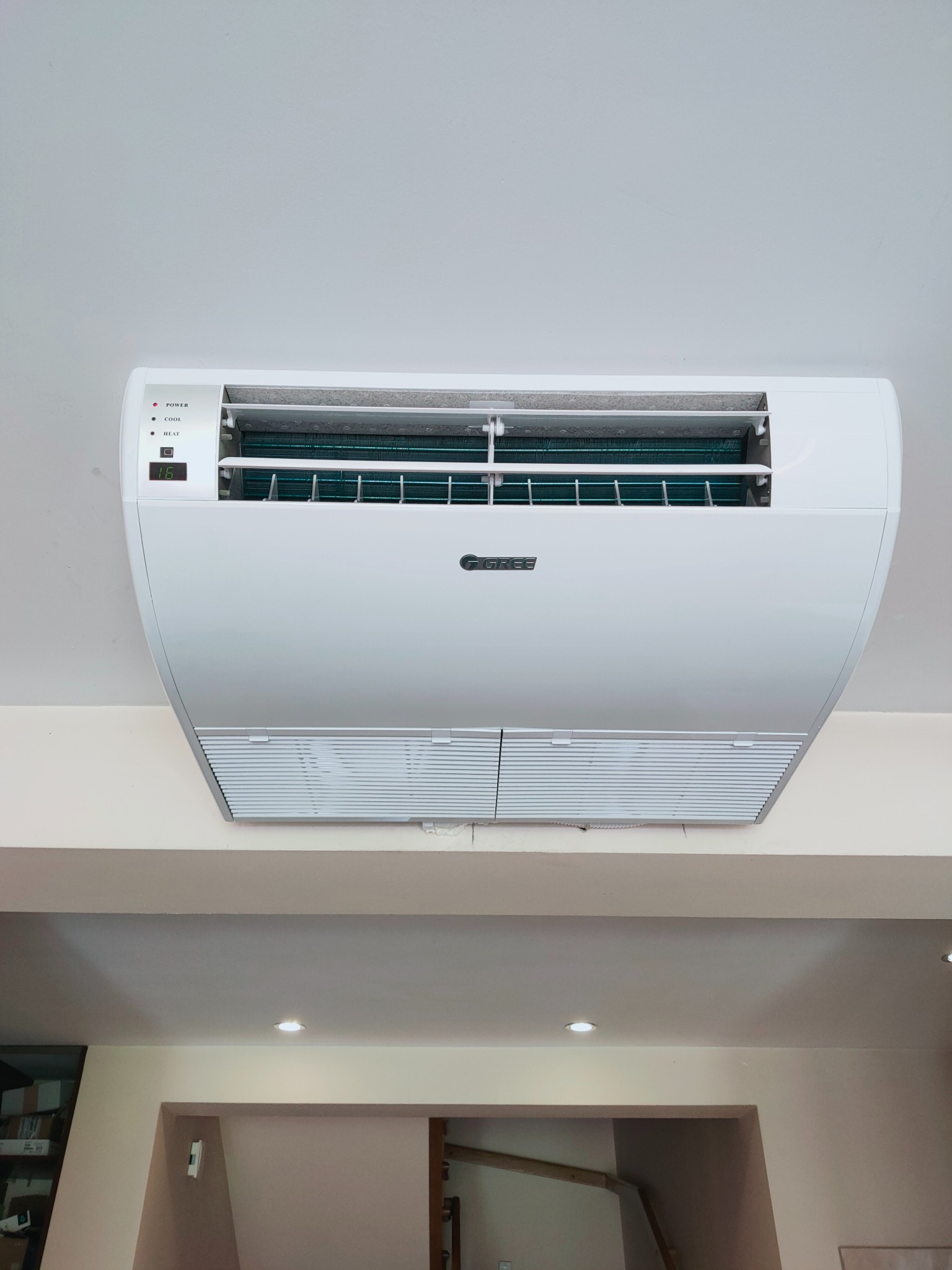 Biała jednostka klimatyzacji marki Gree zamontowana na suficie w pomieszczeniu w Krakowie, widoczny wyświetlacz z temperaturą 16 stopni Celsjusza.