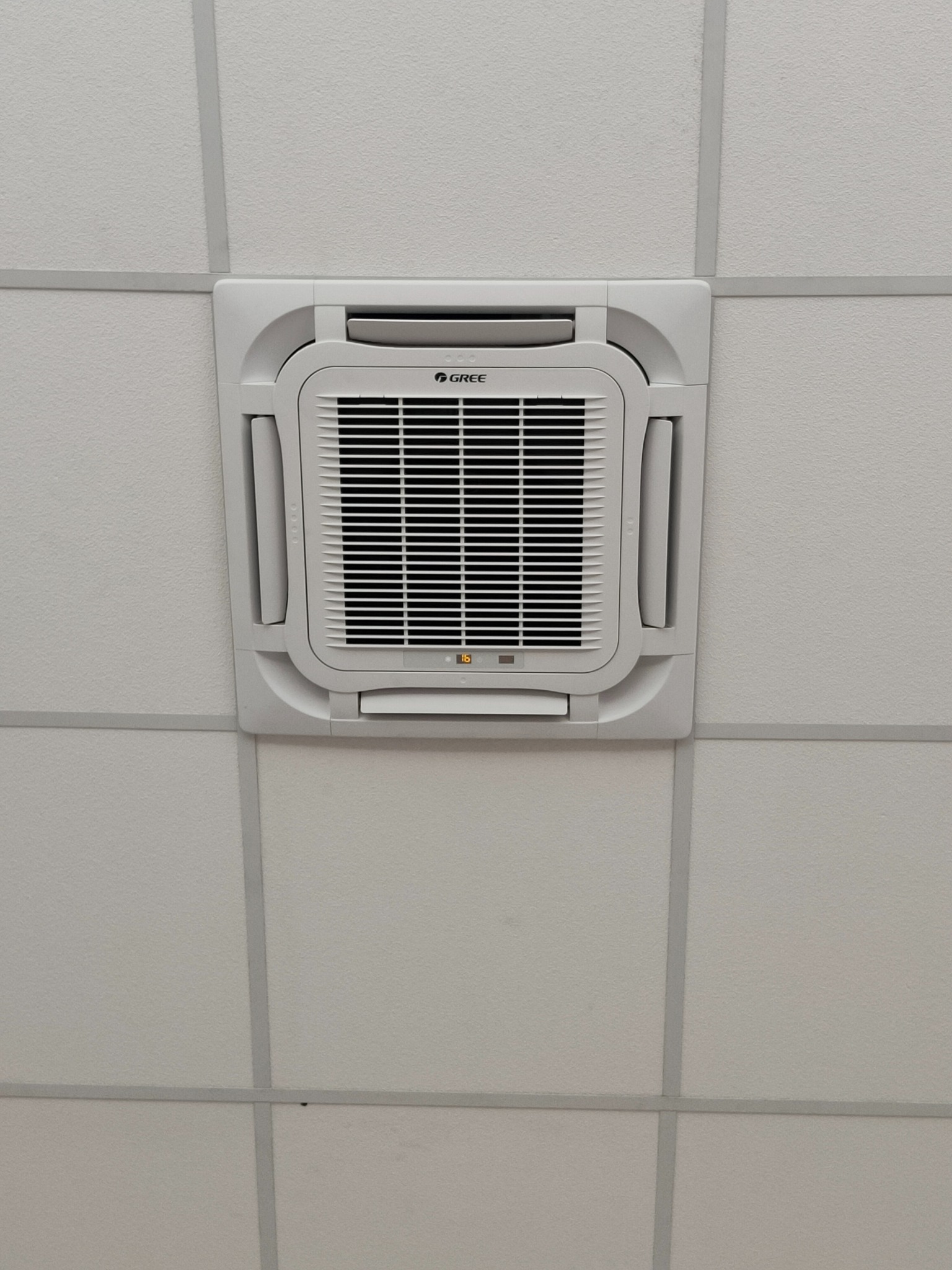 Klimatyzator kasetonowy marki Gree zamontowany w suficie podwieszanym, widoczny wyświetlacz temperatury.