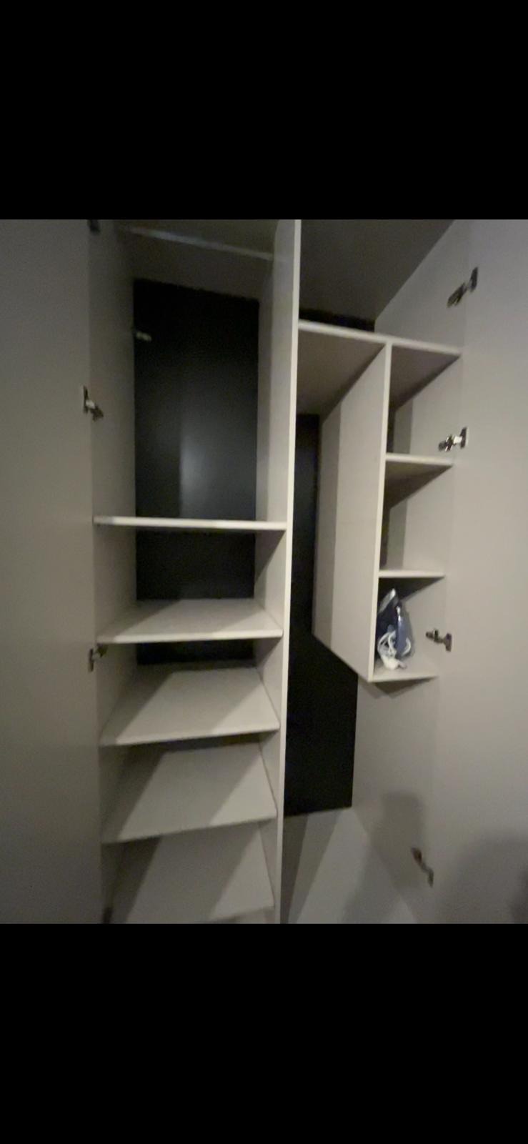 Wnętrze szafy z otwartymi drzwiami, widoczne półki i wnęka z ciemnym tłem, żelazko na półce.