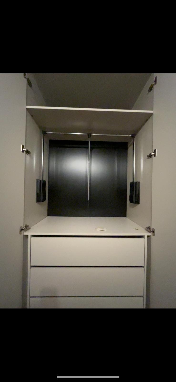 Wnętrze szafy z dwoma szufladami, drążkiem na ubrania i podnośnikiem, widoczne zawiasy drzwi.