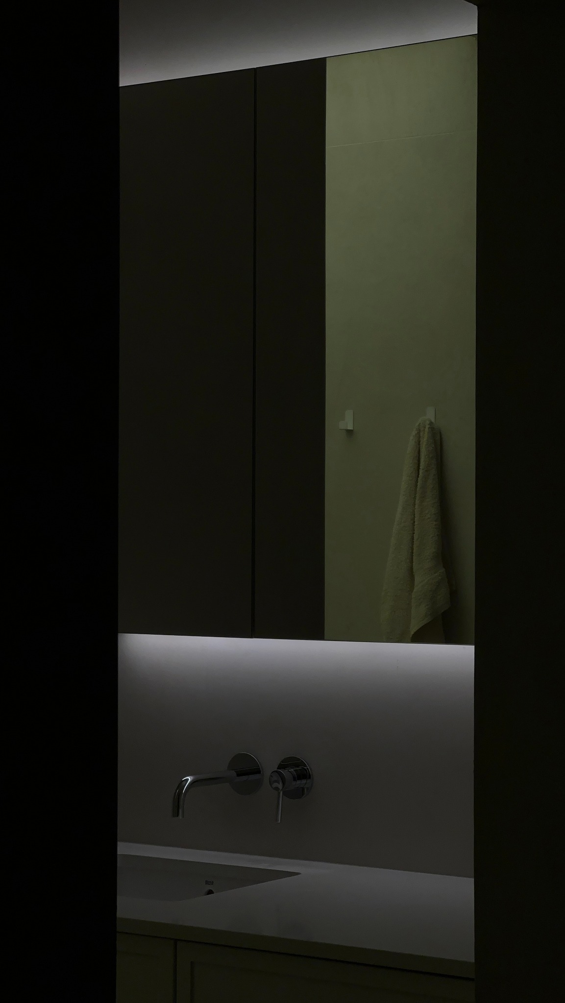 Minimalistyczna łazienka z podświetlanym lustrem szafkowym, chromowaną armaturą ścienną i ręcznikiem na haczyku.