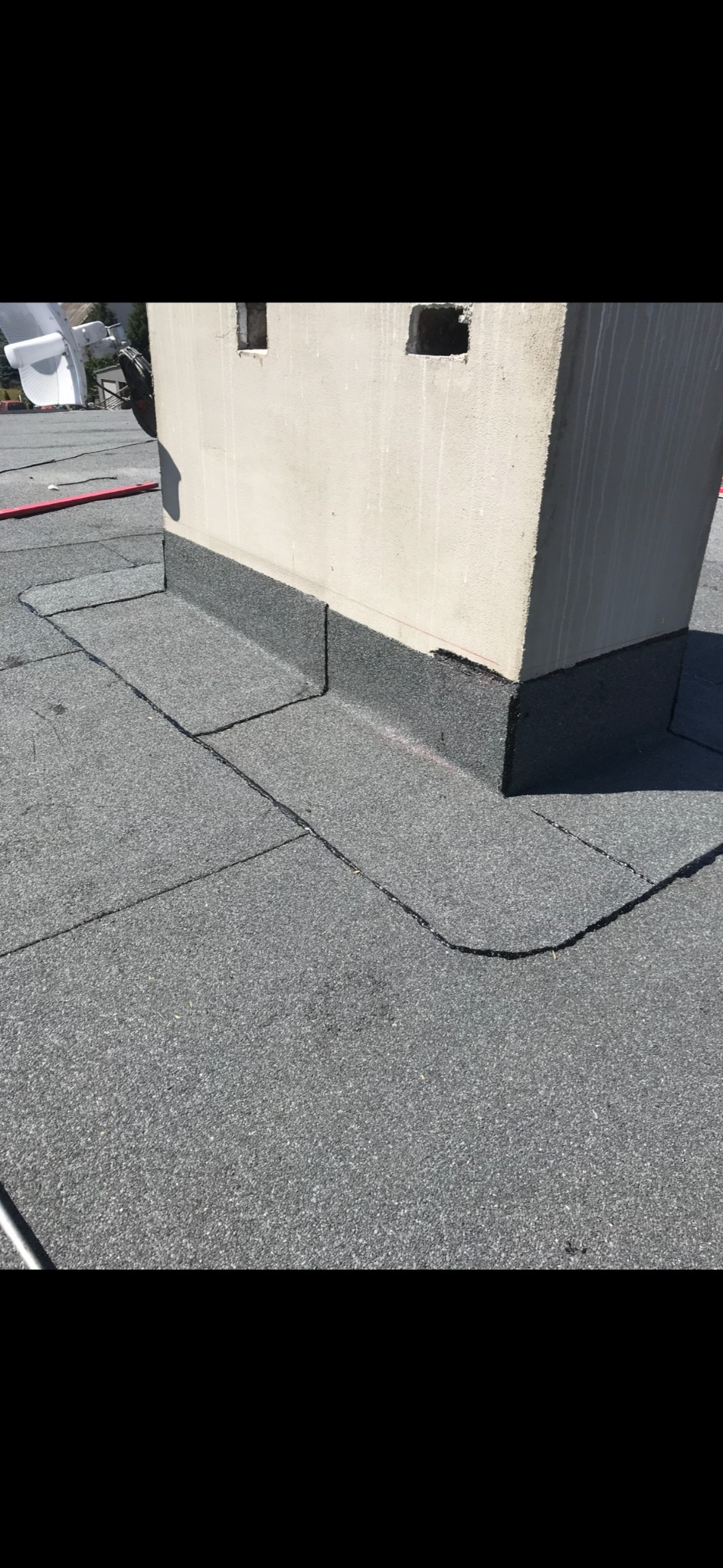 Szczegółowe ujęcie dachu pokrytego papą wokół komina, z widocznymi łączeniami i obróbkami blacharskimi. Jasne oświetlenie podkreśla fakturę materiału.