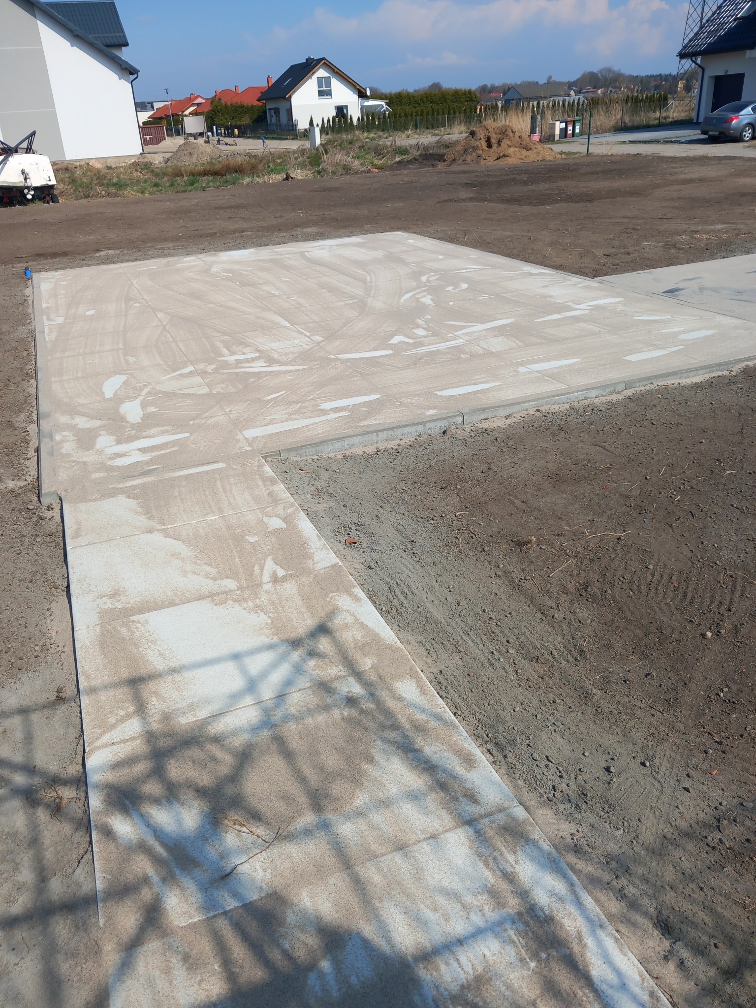Wykończona, jasna powierzchnia z kostki brukowej na posesji, widok z góry. W tle domy jednorodzinne i trawnik. Ślady piasku na kostce.