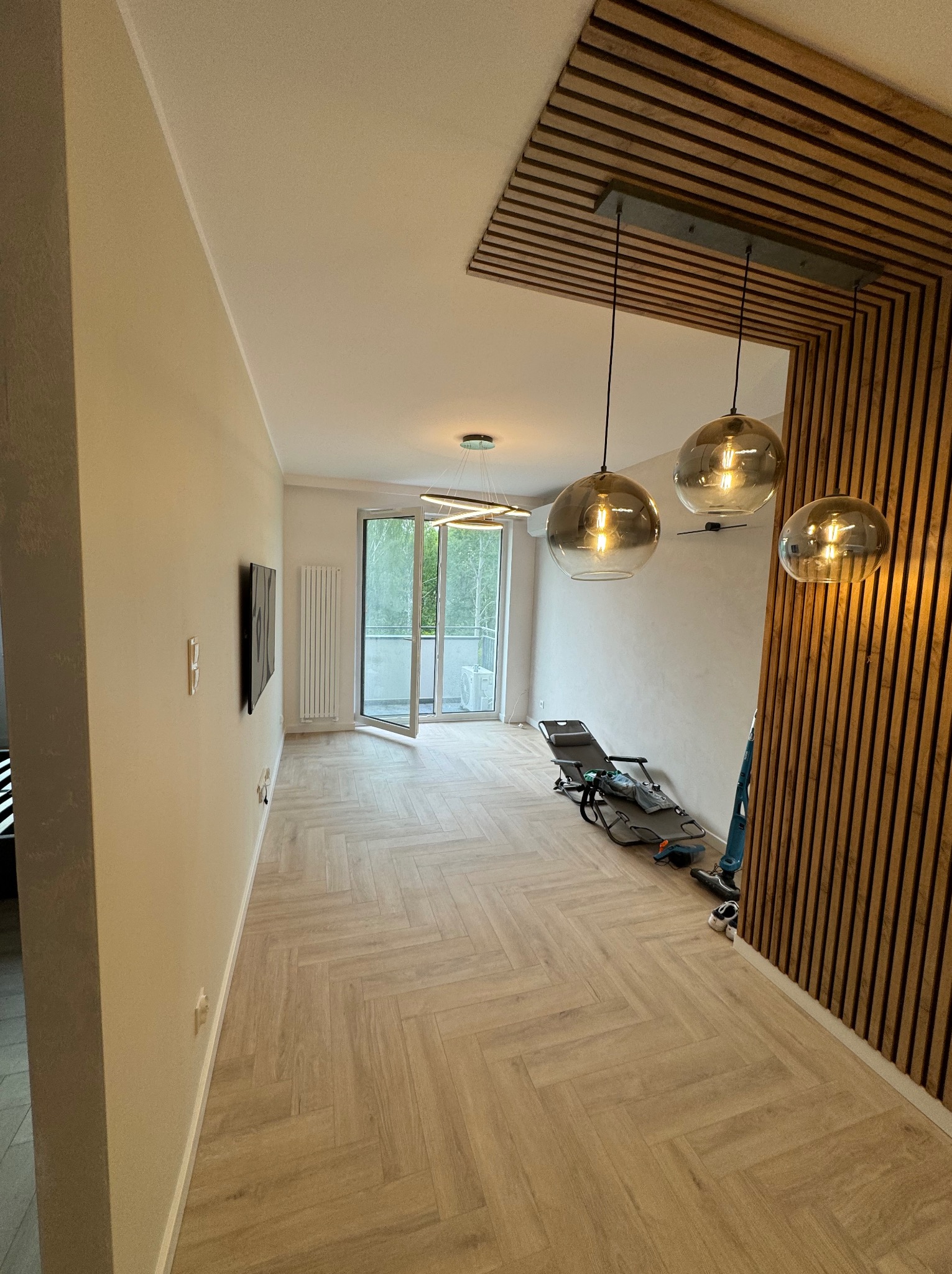 Nowoczesne wnętrze w trakcie prac wykończeniowych: parkiet ułożony we wzór jodełki, drewniana dekoracja na suficie z trzema okrągłymi lampami, ściany przygotowane pod malowanie, widoczne narzędzia...