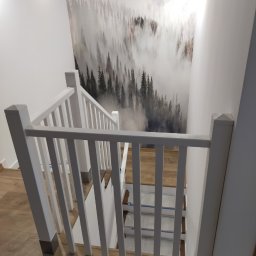 VOK - Biała balustrada schodów z widokiem na fototapetę z motywem mglistego lasu i sylwetkami ptaków, drewniana podłoga.