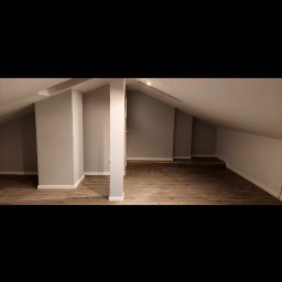 VOK - Poddasze po remoncie: szare ściany, drewnopodobna podłoga, białe listwy przypodłogowe, widoczne skosy i kolumna konstrukcyjna.