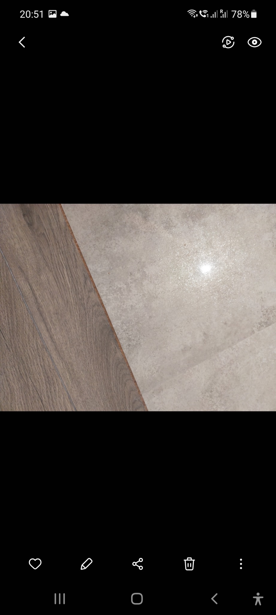 Połączenie paneli podłogowych imitujących drewno z szarą, matową płytką ceramiczną, widoczne z bliska na podłodze.