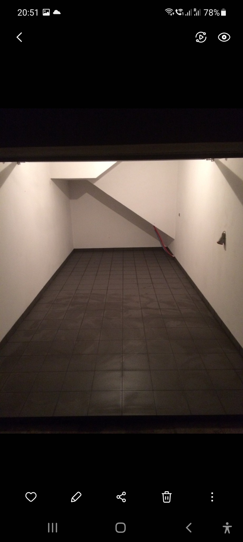 Wykafelkowana podłoga w pustym pomieszczeniu z białymi ścianami i widocznymi schodami w tle, oświetlona światłem z góry.