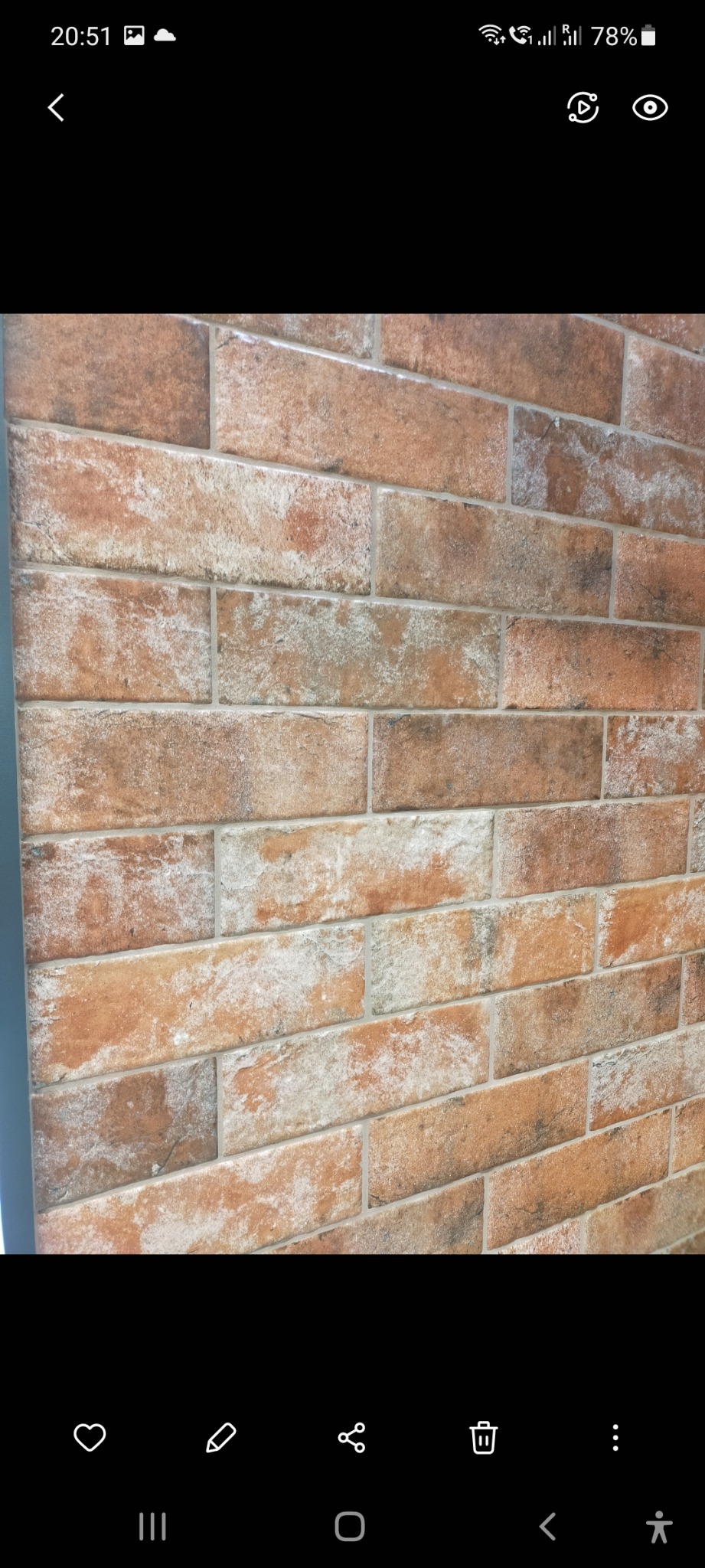 Ściana wyłożona ceglastymi płytkami imitującymi cegłę, z wyraźnymi fugami i delikatną fakturą.