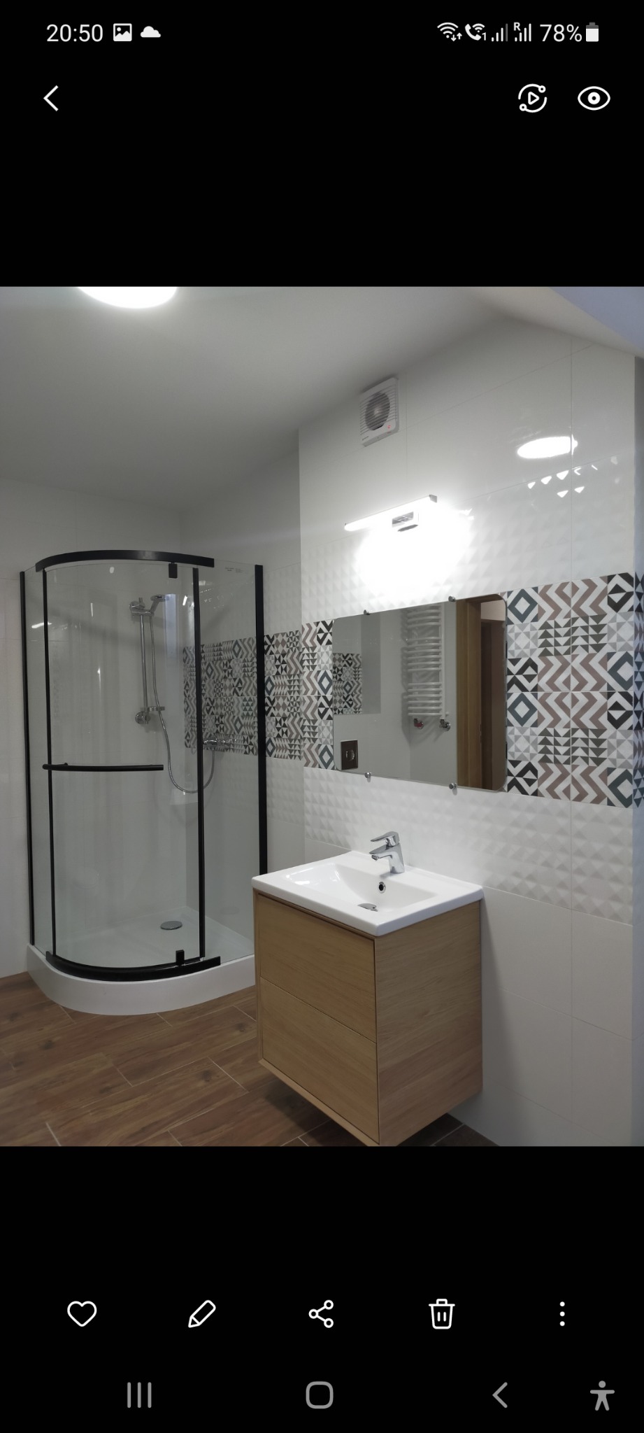 Nowoczesna łazienka z kabiną prysznicową z czarnymi ramami, umywalką z drewnianą szafką i wzorzystymi płytkami na ścianie.