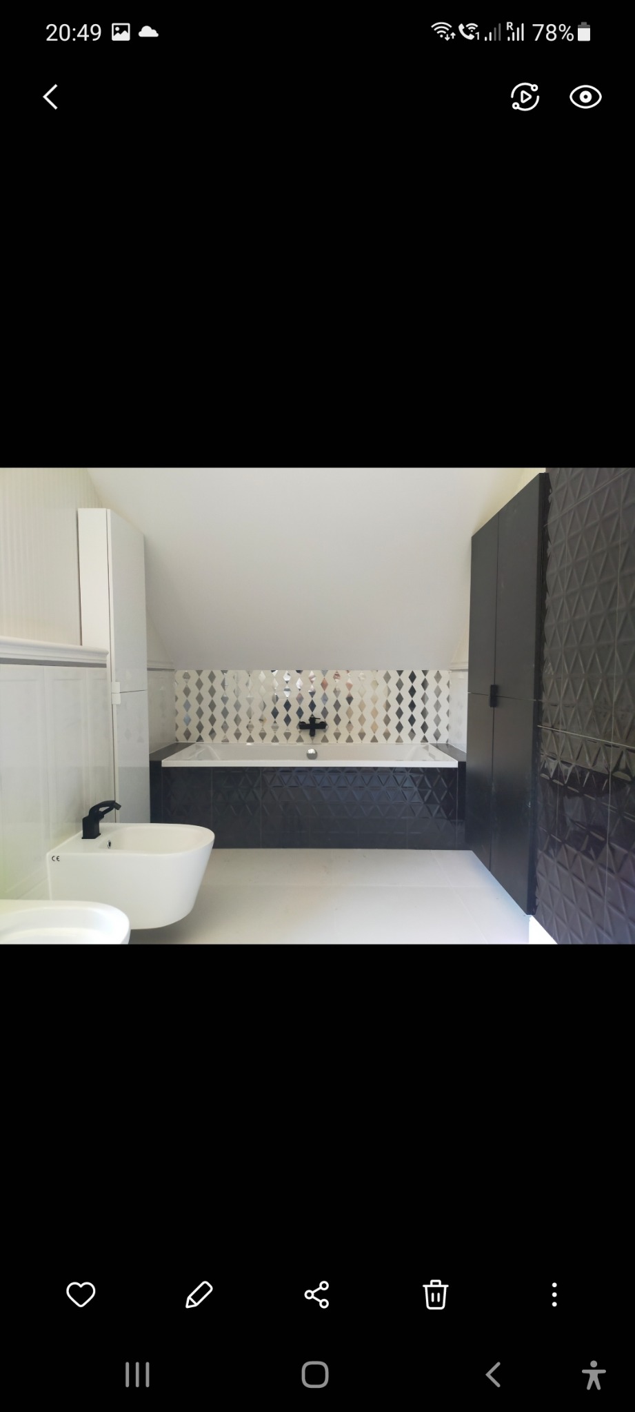 Nowoczesna łazienka z białą podłogą, bidetem z czarną armaturą, wanną obudowaną czarnymi płytkami z trójwymiarowym wzorem oraz ścianą z mozaiki w romby.