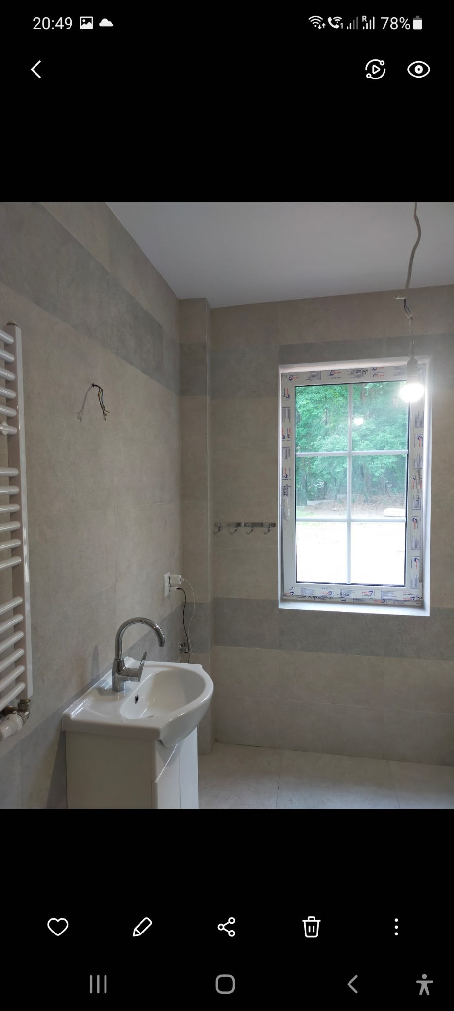 Wykończona łazienka z szarymi płytkami, białą umywalką z szafką i grzejnikiem drabinkowym, widoczne niedokończone podłączenie elektryczne do oświetlenia.