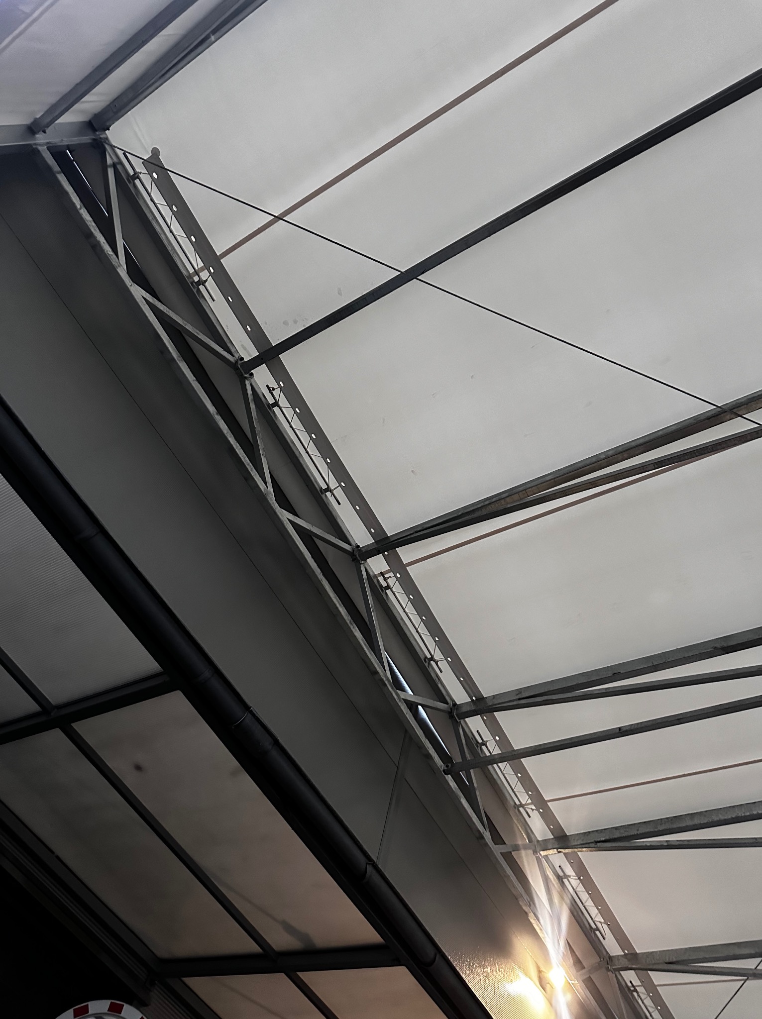 Wnętrze hali z widoczną konstrukcją stalową dachu i płytami warstwowymi, oświetlone od dołu.