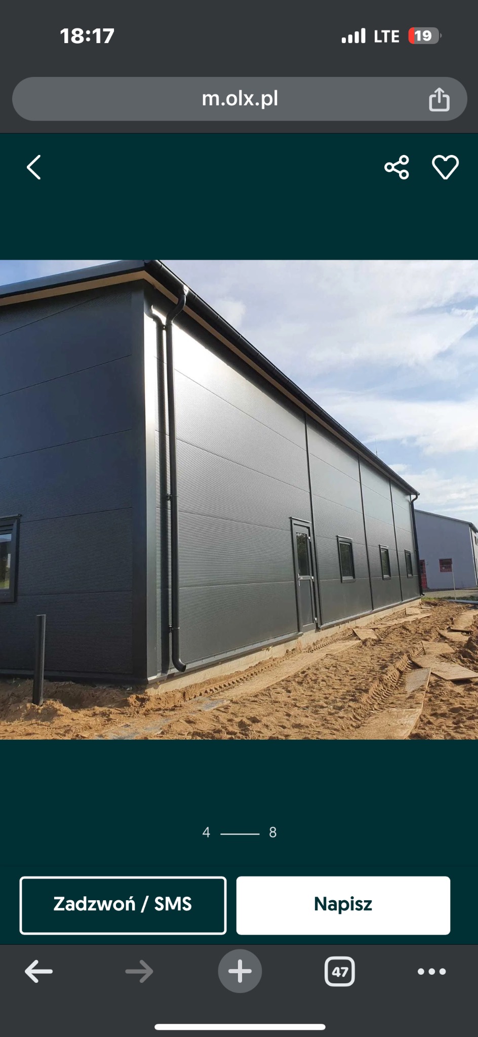 Gotowa hala przemysłowa z szarej płyty warstwowej, widok z zewnątrz, z widocznymi oknami i drzwiami, teren wokół w trakcie prac ziemnych.