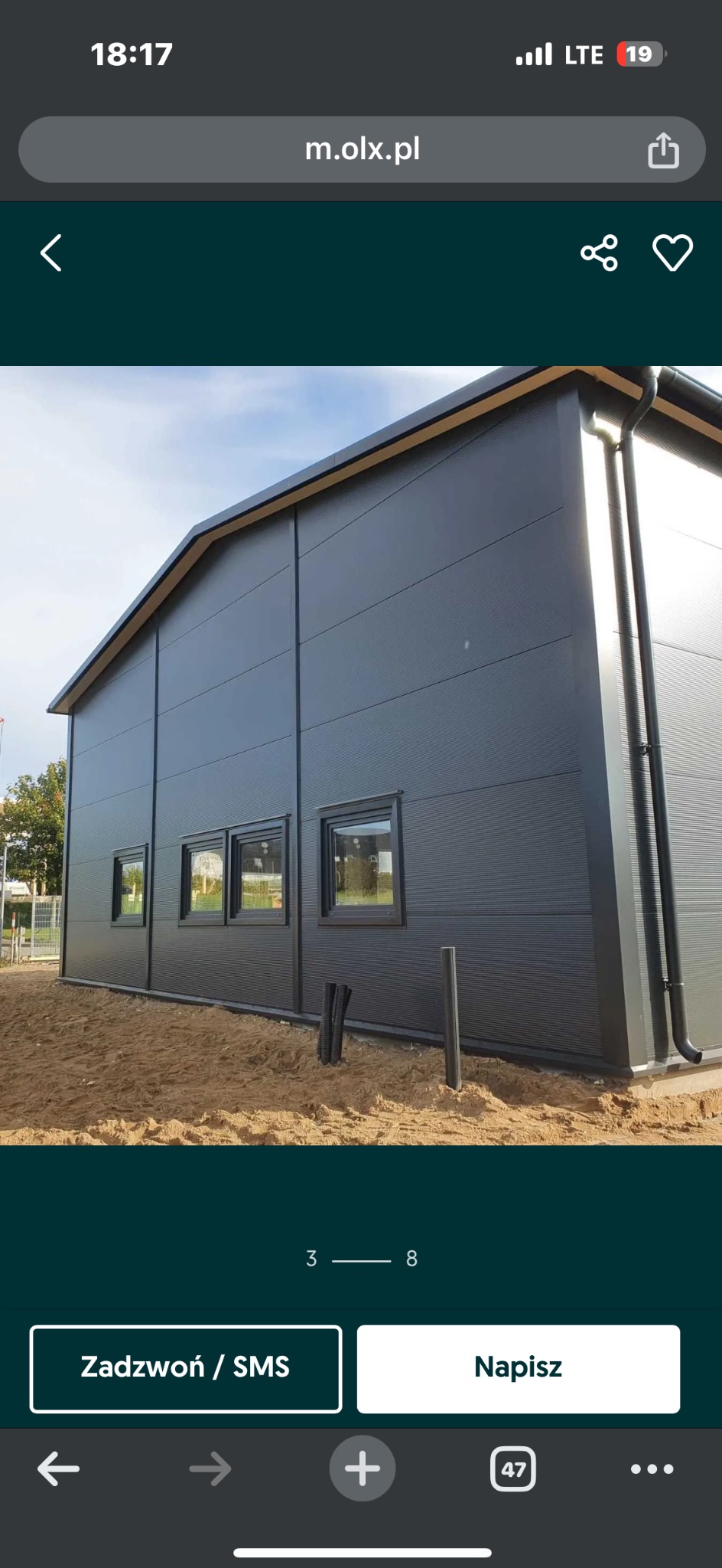 Zewnętrzny widok hali z szarej płyty warstwowej z trzema oknami, widoczne rury spustowe i teren przygotowany pod zagospodarowanie.