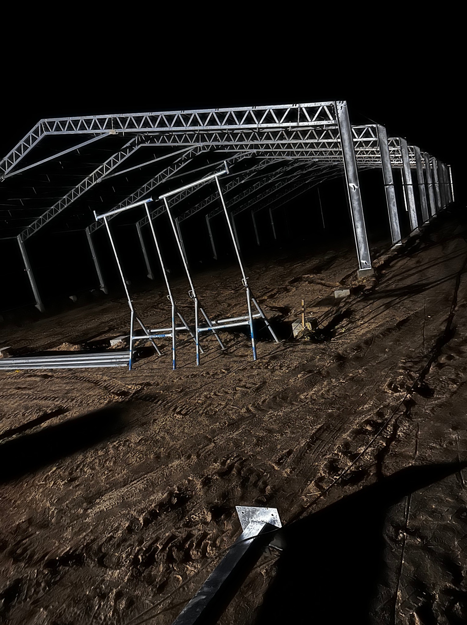 Nocny widok na budowę hali z widoczną konstrukcją stalową, podpory montażowe i przygotowany teren.