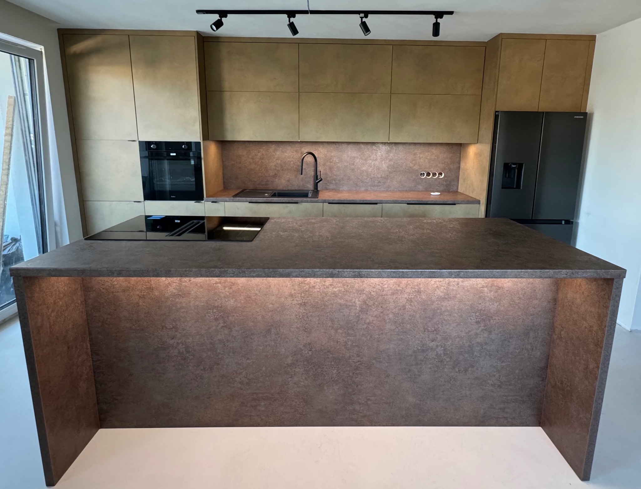 Nowoczesna kuchnia z wyspą i frontami w odcieniach brązu i beżu, czarne AGD, oświetlenie punktowe.