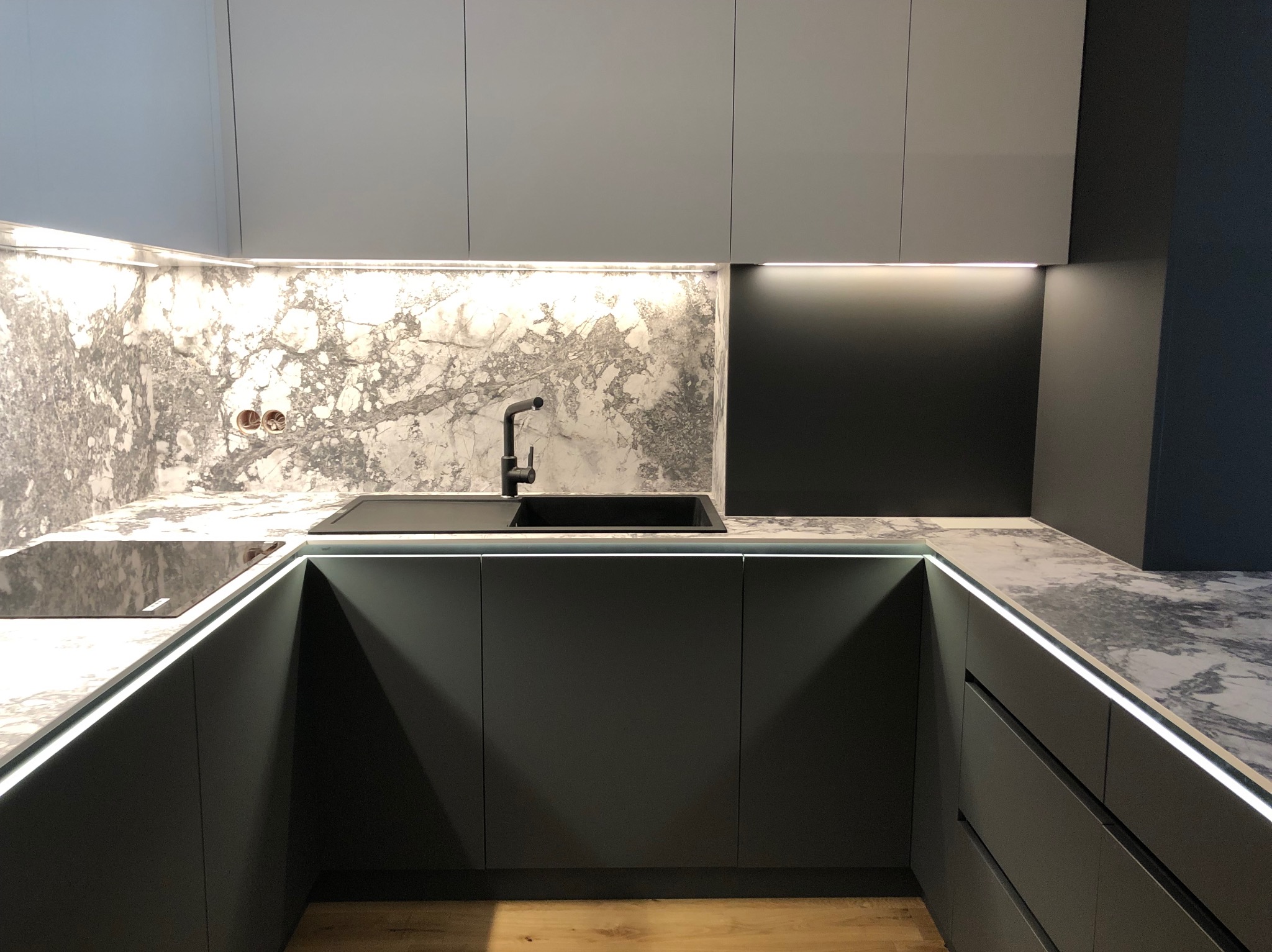 Nowoczesna kuchnia z szarymi frontami, marmurowym blatem i podświetleniem LED, czarna armatura i płyta indukcyjna.