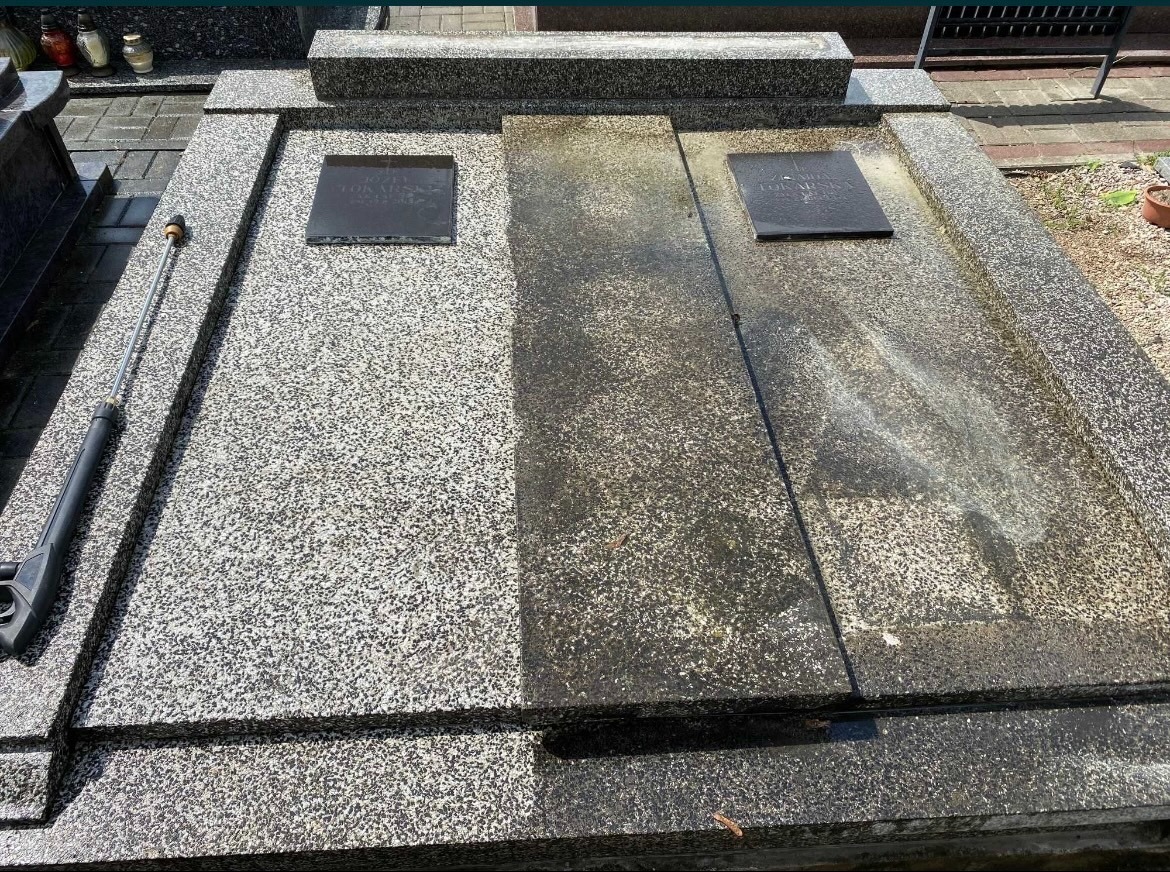 Granitowy nagrobek częściowo wyczyszczony, widoczna różnica w kolorze i czystości między wyczyszczoną a brudną powierzchnią, lanca myjki ciśnieniowej leży obok.