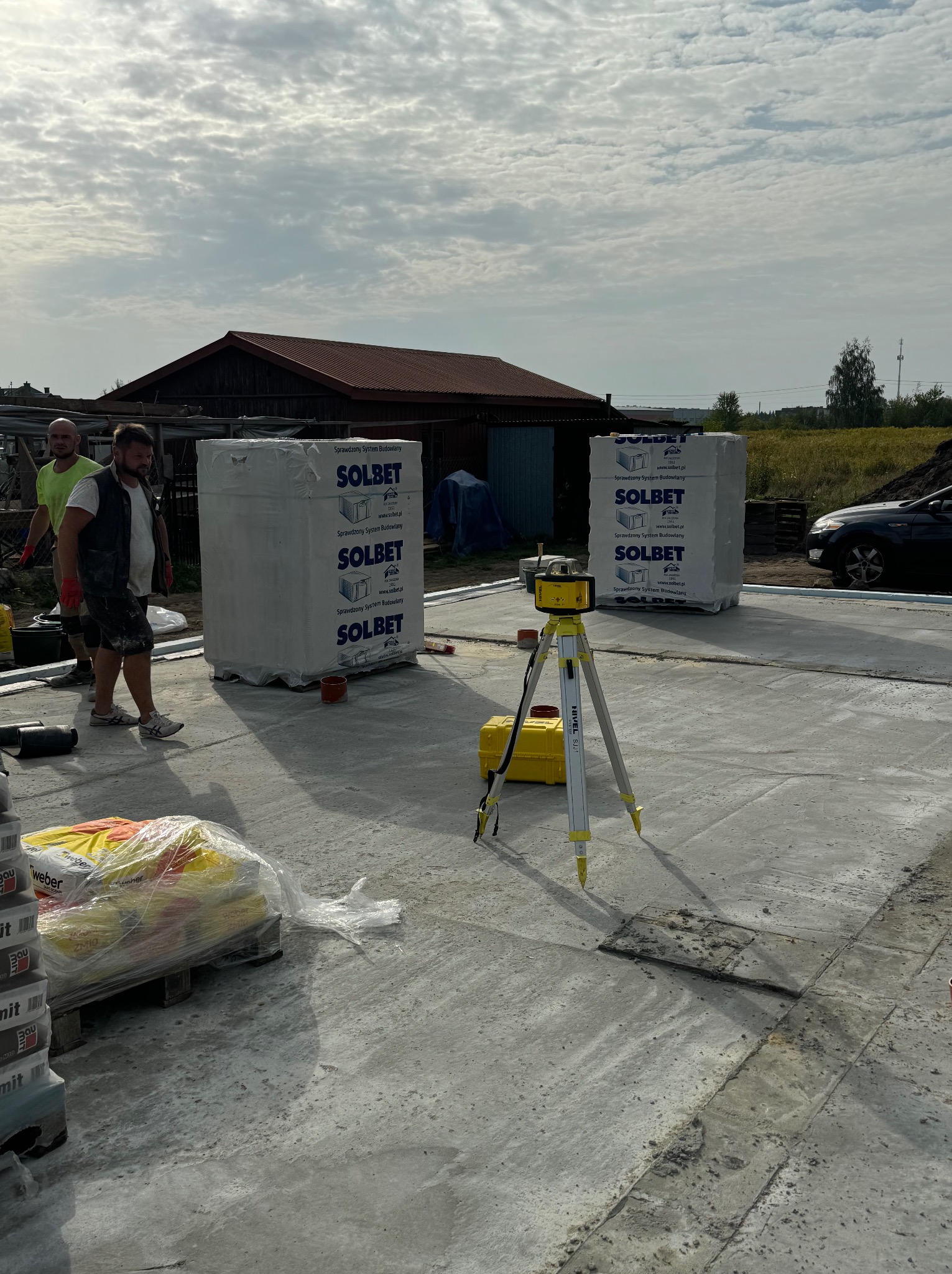 Wyrównana płyta fundamentowa z widocznymi blokami Solbet, niwelatorem laserowym i pracownikami w tle, przygotowana pod budowę domu.