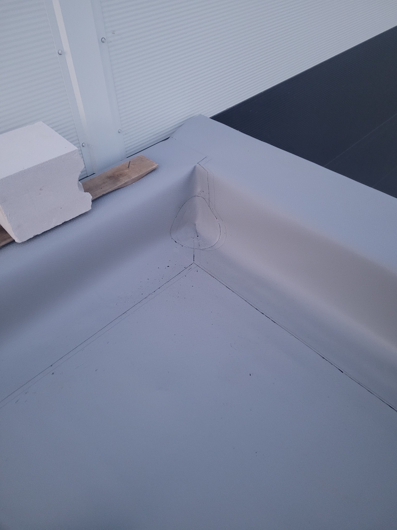 Szary, płaski dach z obróbką blacharską w narożniku, widoczny fragment ściany z blachy trapezowej i bloczek z betonu komórkowego.