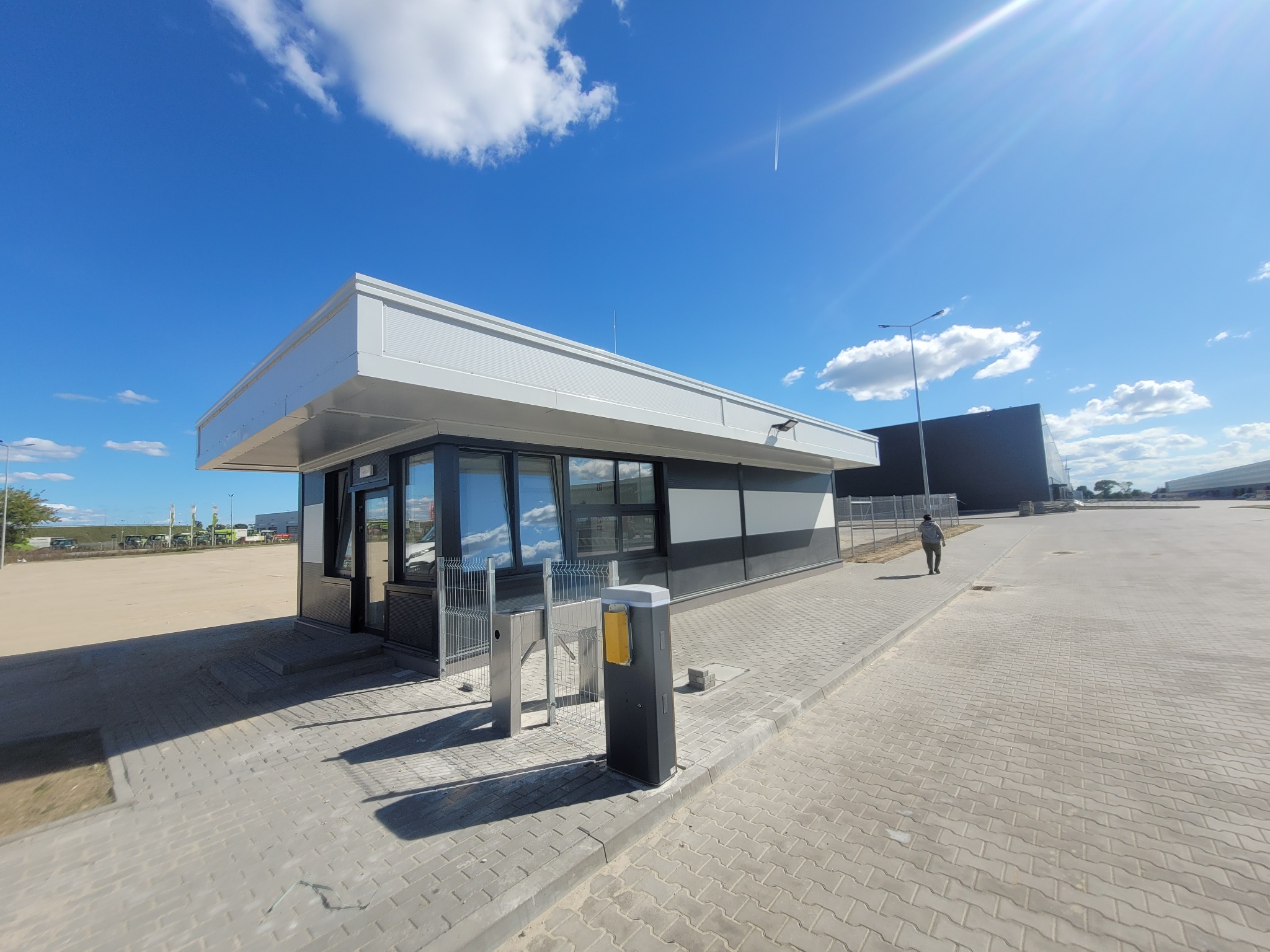 Nowoczesny, biało-czarny budynek portierni z płaskim dachem, widoczny z zewnątrz na tle błękitnego nieba i placu manewrowego.