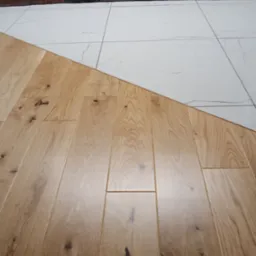 Połączenie jasnego parkietu z białymi płytkami imitującymi marmur i fragmentem ściany z cegły klinkierowej w tle.