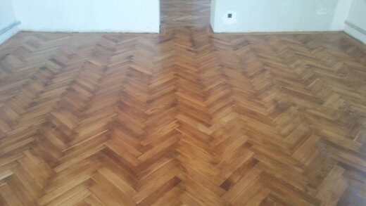 Ułożony parkiet w jodełkę, widok z góry na jasne drewno, ściany w tle przygotowane do malowania.