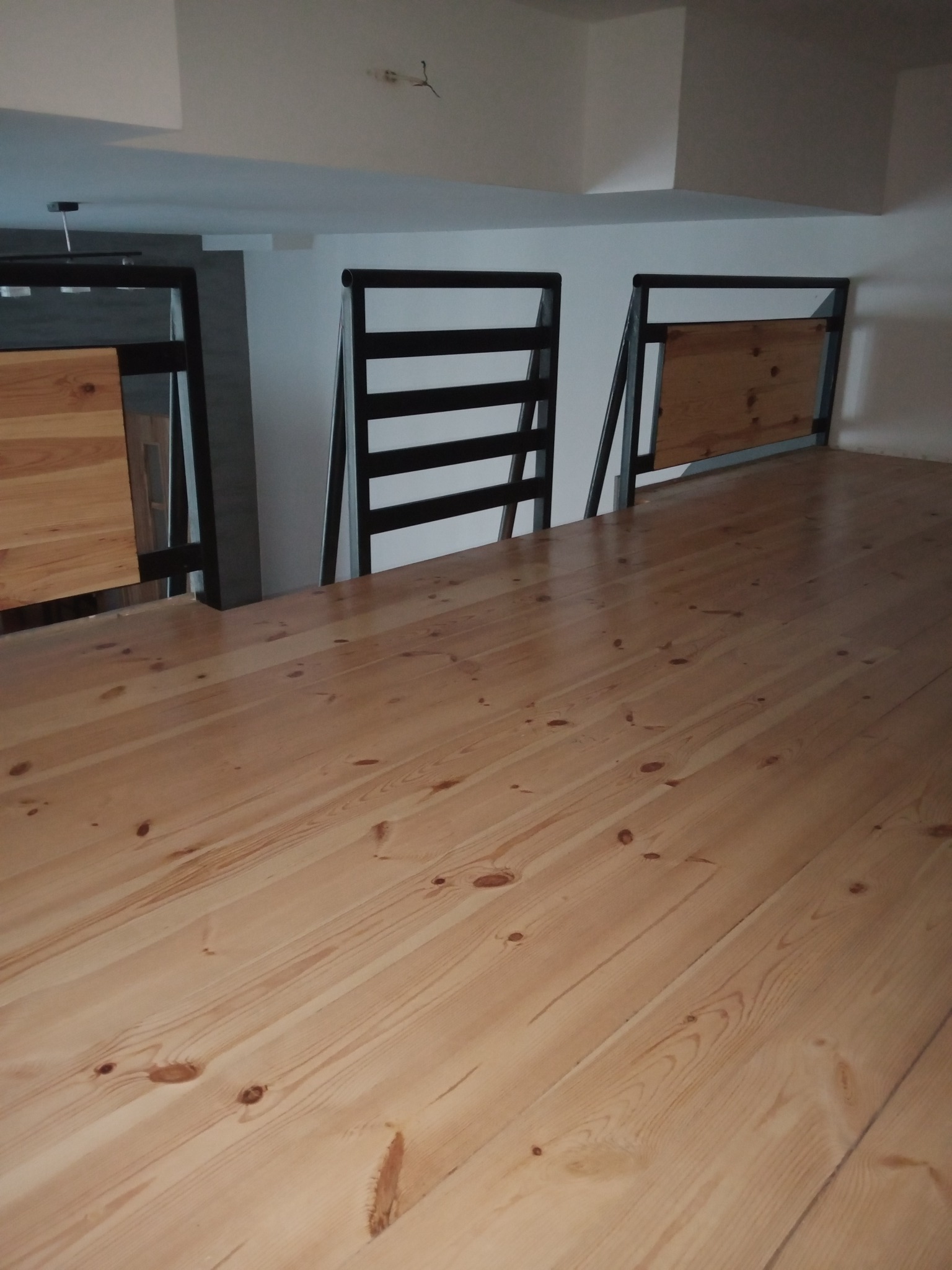 Jasna, drewniana podłoga z widoczną strukturą drewna i czarnymi elementami konstrukcyjnymi w tle, oświetlona z góry