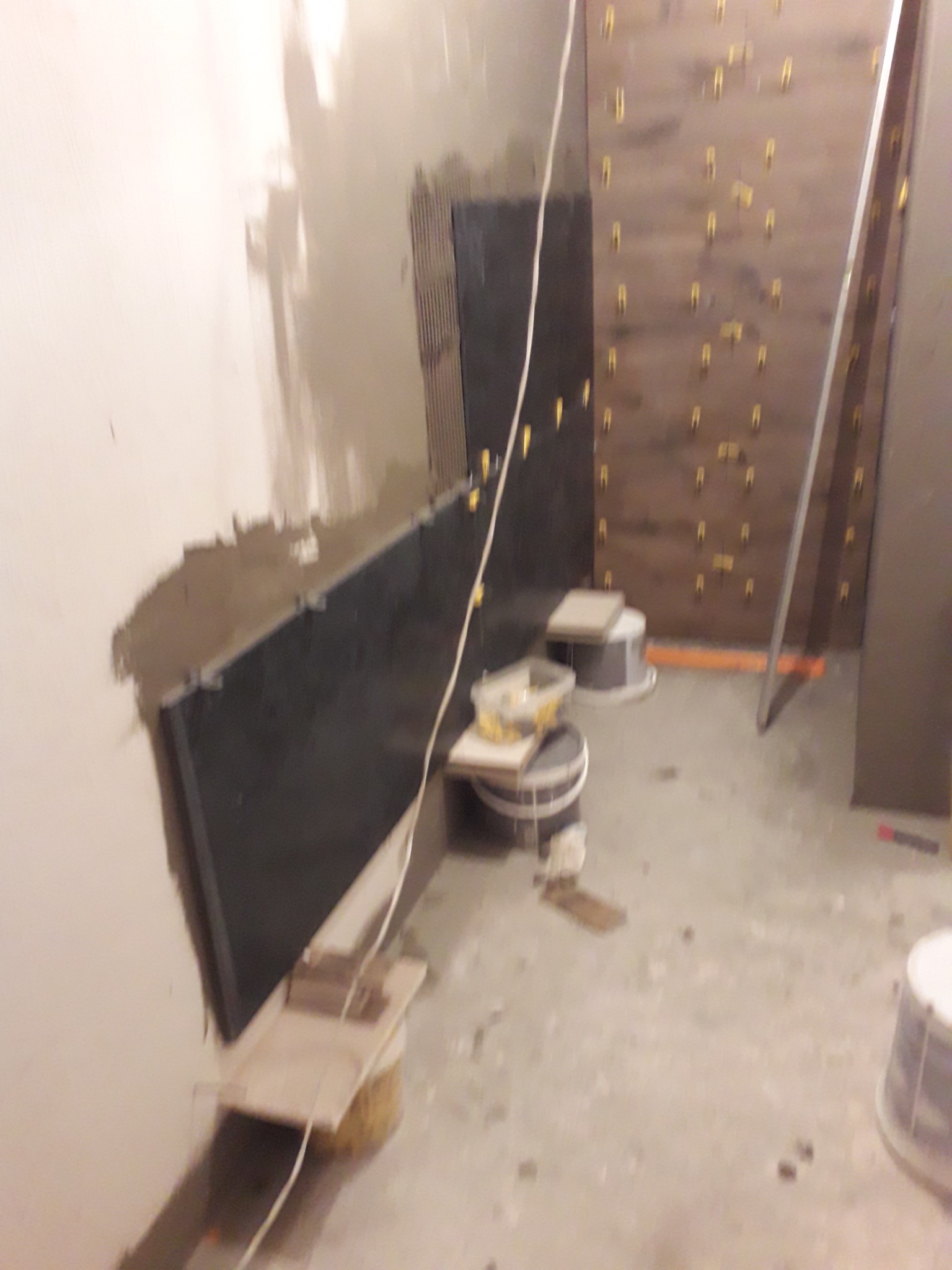 Montaż ciemnych płytek na ścianie w trakcie prac wykończeniowych, widoczne narzędzia, poziomica i krzyżyki dystansowe.