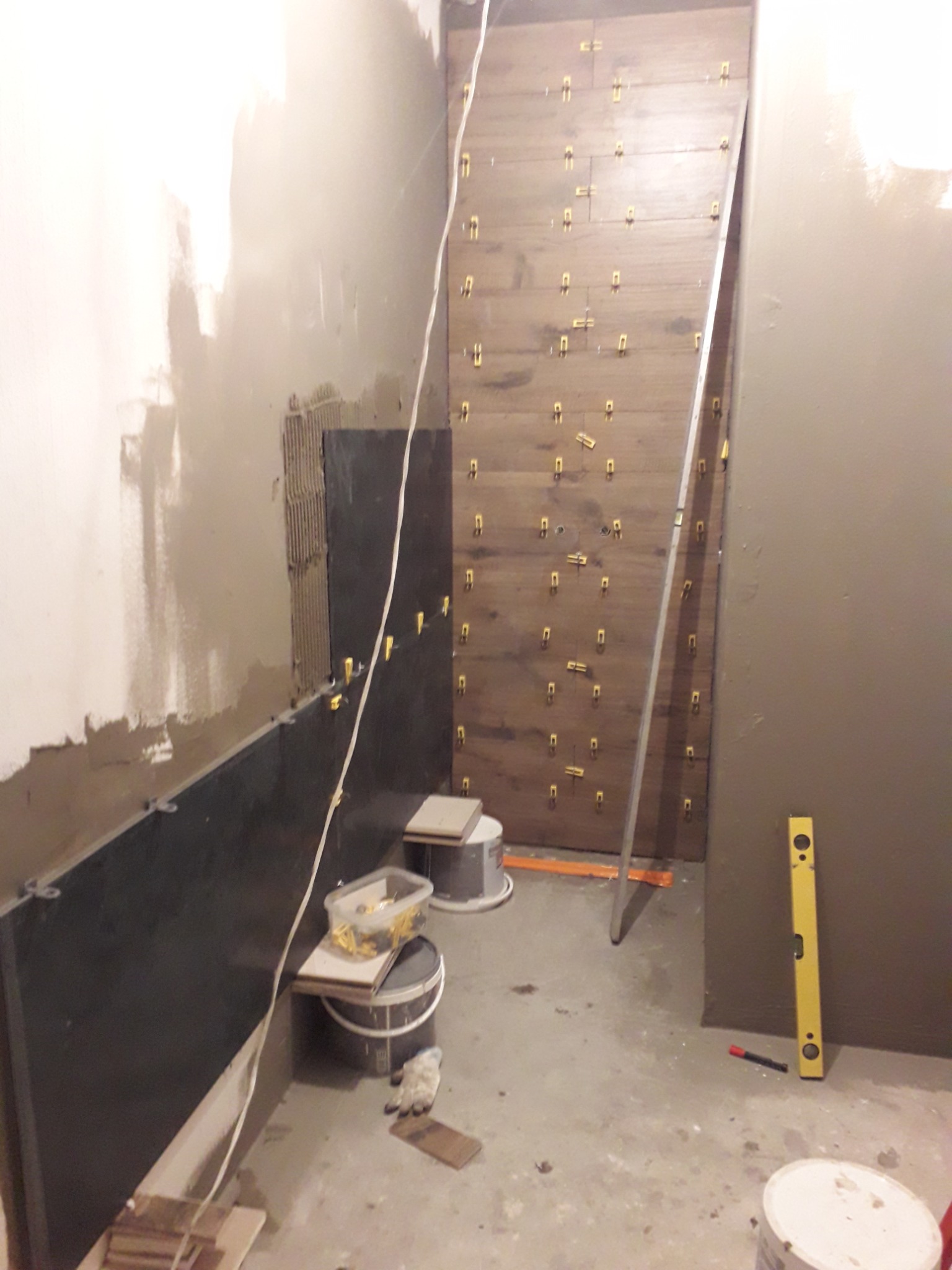 Układanie płytek imitujących drewno na ścianie w Suwałkach, widoczne poziomice, zaprawa i plastikowe krzyżyki dystansowe.