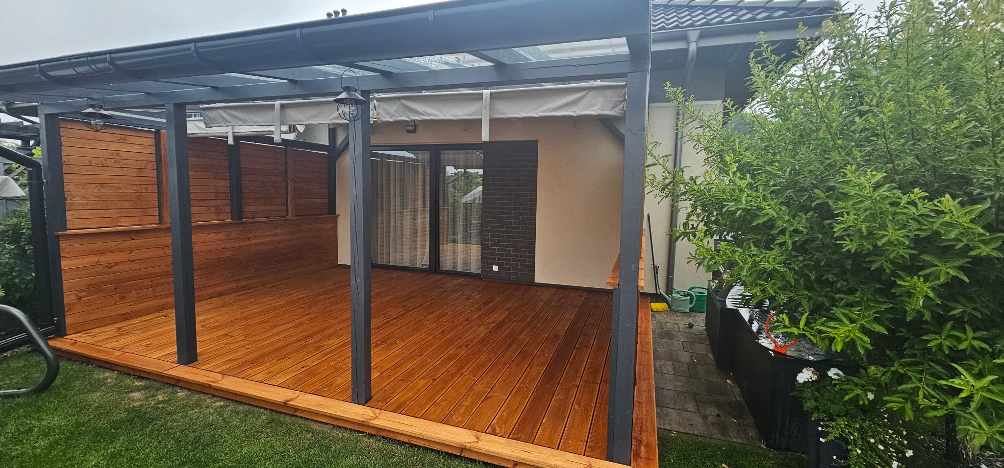 Taras z drewna skandynawskiego w kolorze palisandrach, zadaszenie szklo, zaciemnienie rolety rzymskie