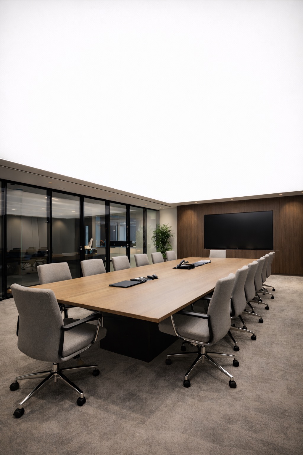 Nowoczesna sala konferencyjna z długim stołem z drewna, szarymi krzesłami na kółkach i podświetlanym sufitem. Na ścianie duży telewizor i drewniane panele.