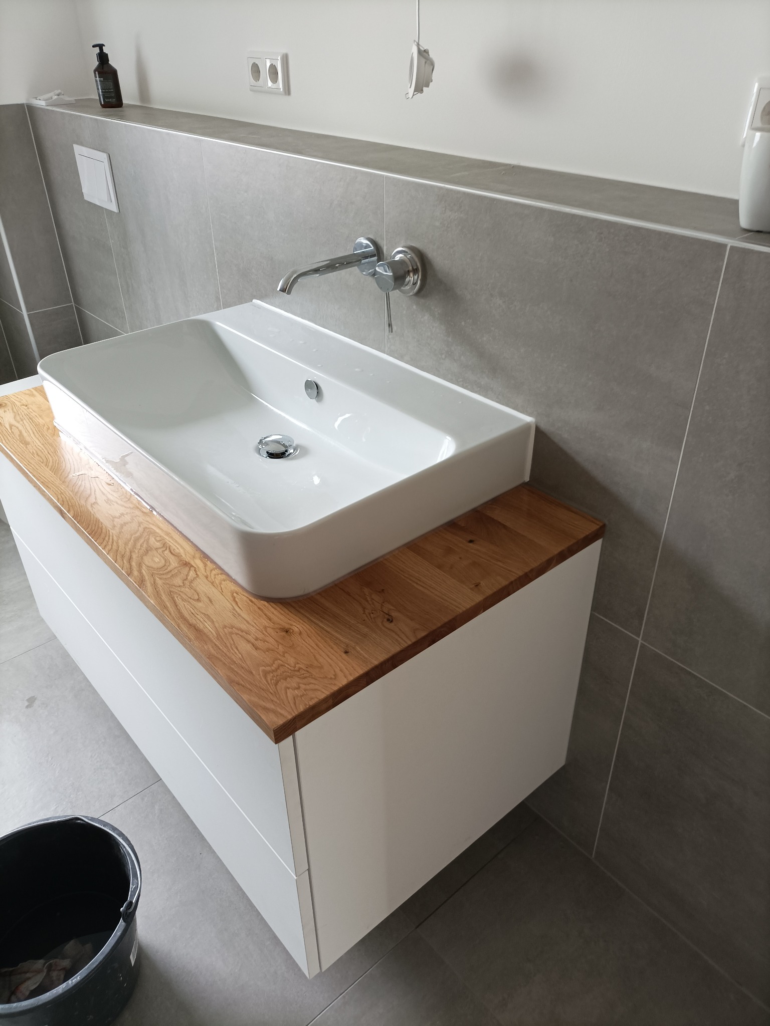 Nowoczesna, prostokątna umywalka nablatowa z chromowaną baterią, osadzona na szafce z drewnianym blatem w łazience w Pustej Woli, wykończonej szarymi płytkami.