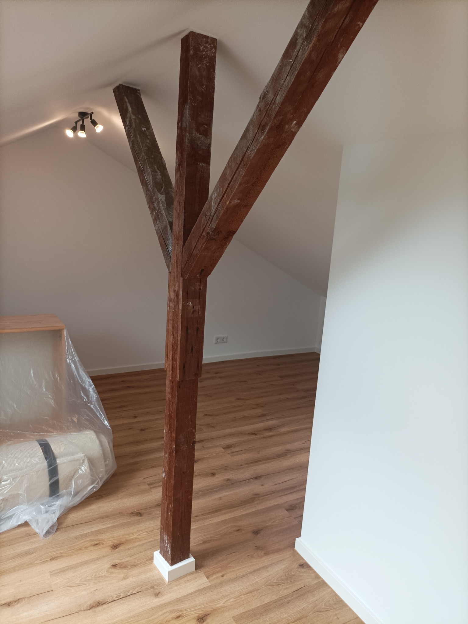 Poddasze po remoncie: drewniana konstrukcja nośna z belek, świeżo pomalowane białe ściany, panele podłogowe imitujące drewno, meble zabezpieczone folią.