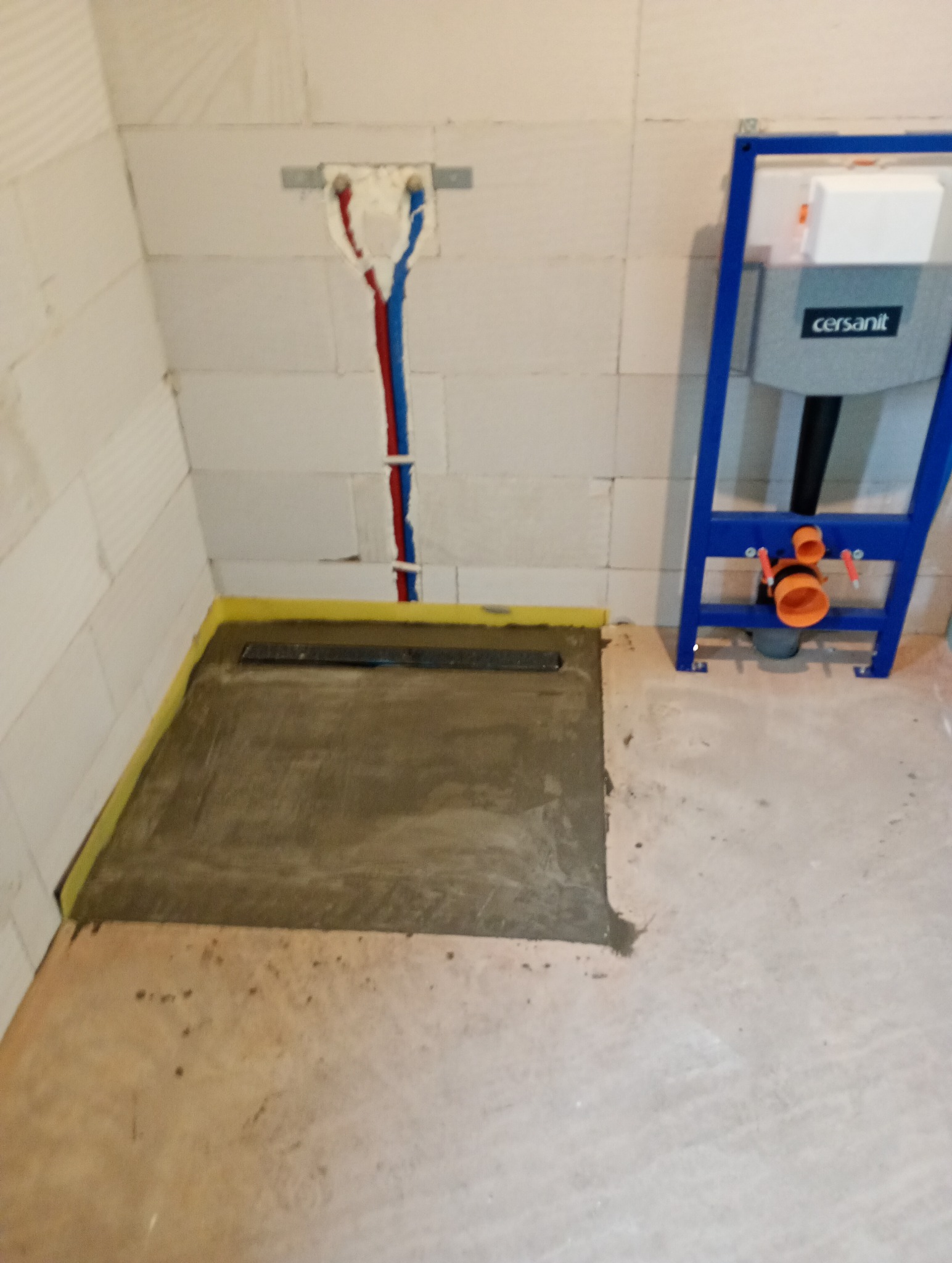 Przygotowanie podłoża pod prysznic typu walk-in z odpływem liniowym, widoczne rury instalacji wodnej i stelaż podtynkowy WC marki Cersanit, ściany z betonu komórkowego.
