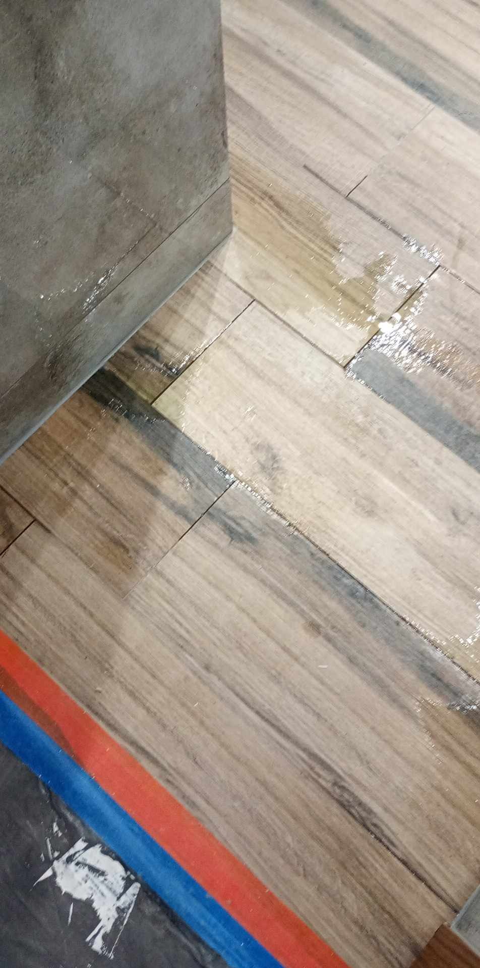 Ułożona, ale jeszcze mokra, podłoga z płytek imitujących drewno w łazience, widoczne ślady fugowania i taśma malarska na podłodze.