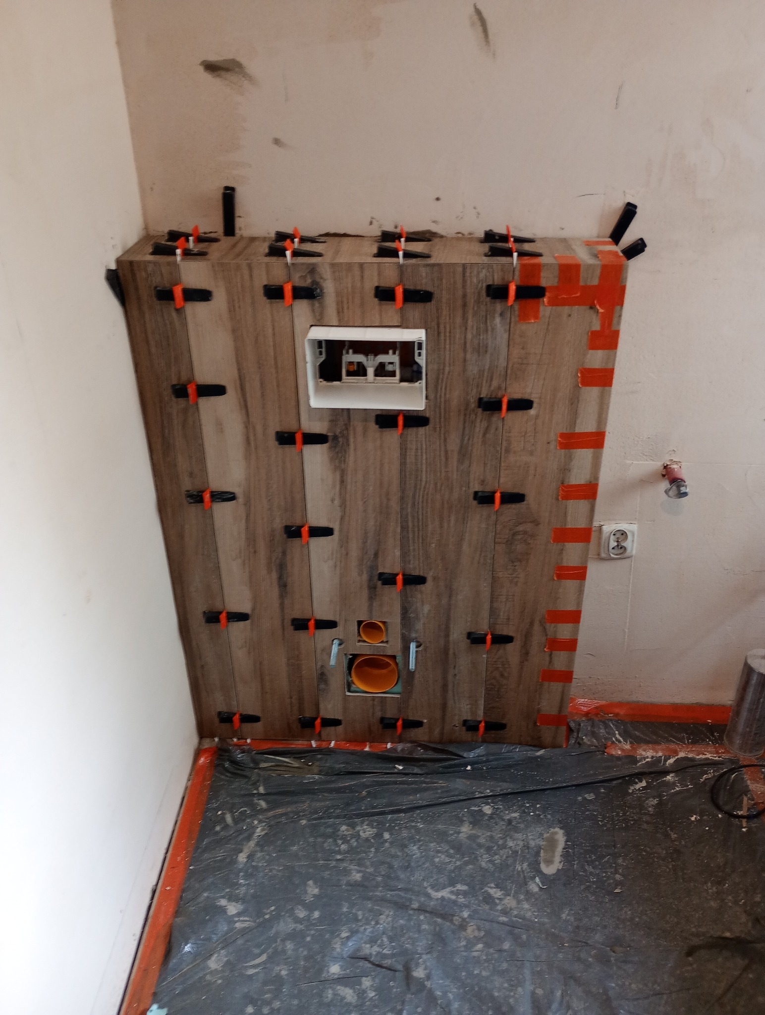 Montaż płytek imitujących drewno na stelażu podtynkowym w łazience z użyciem klipsów poziomujących, widoczne instalacje wodno-kanalizacyjne.