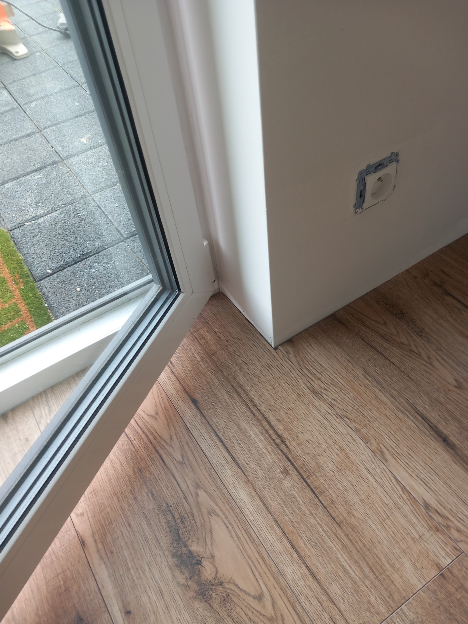 Fragment wnętrza w Witowie po remoncie: ściana z gładzią, drewnopodobna podłoga, okno i puszka elektryczna w ścianie.