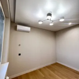 Pomalowane na beżowo puste wnętrze z drewnianą podłogą, nowoczesnym oświetleniem sufitowym i zamontowanym klimatyzatorem.