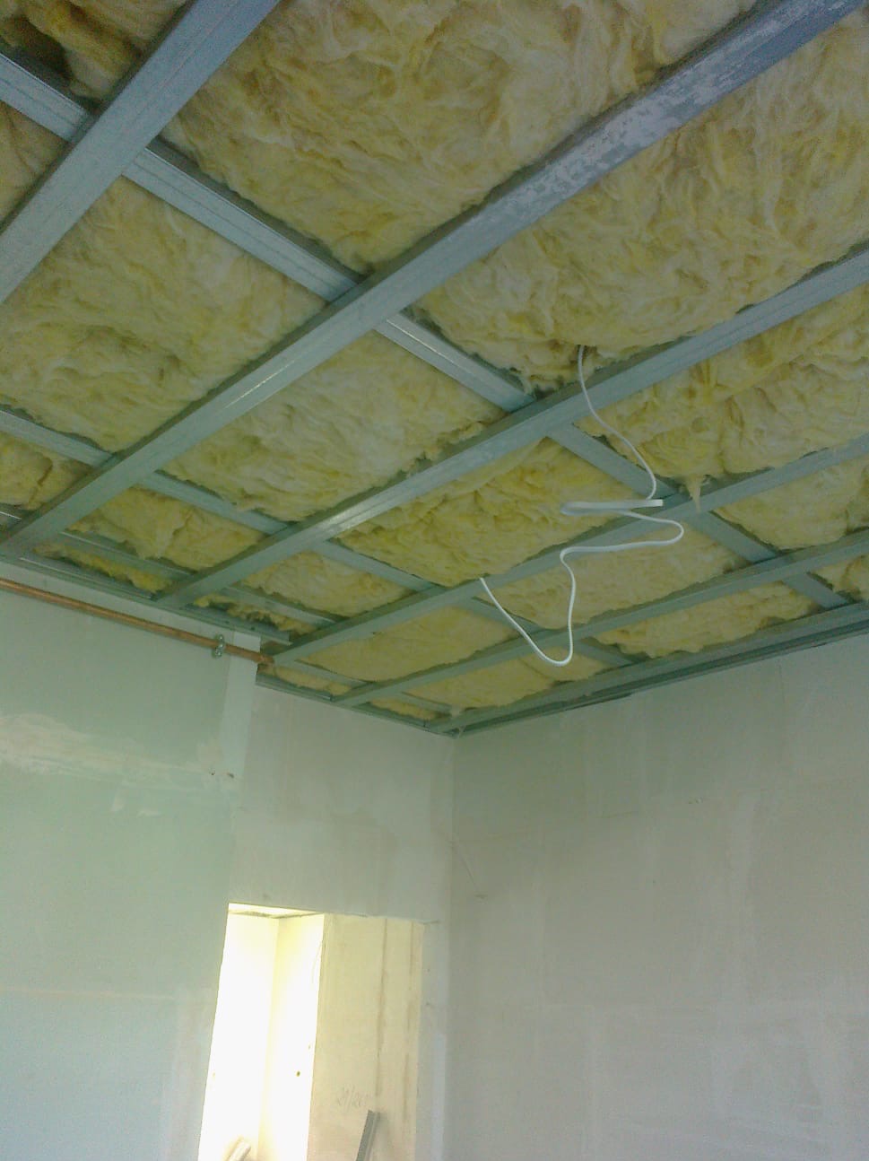 Sufit podwieszany z izolacją z wełny mineralnej, widoczne kable elektryczne i fragment ściany po szpachlowaniu, przygotowane do dalszych prac wykończeniowych.