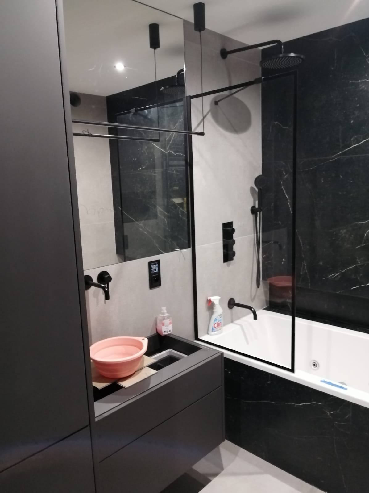 Nowoczesna łazienka z czarnymi akcentami: marmurowe płytki, czarna armatura, szklana kabina prysznicowa i umywalka z różową miską.