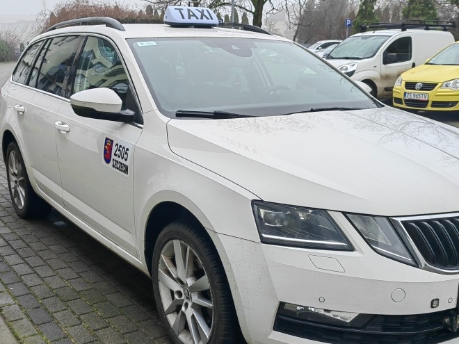 Biała taksówka kombi marki Skoda z numerem bocznym 2505 Szczecin, zaparkowana na chodniku, na dachu podświetlony napis TAXI.