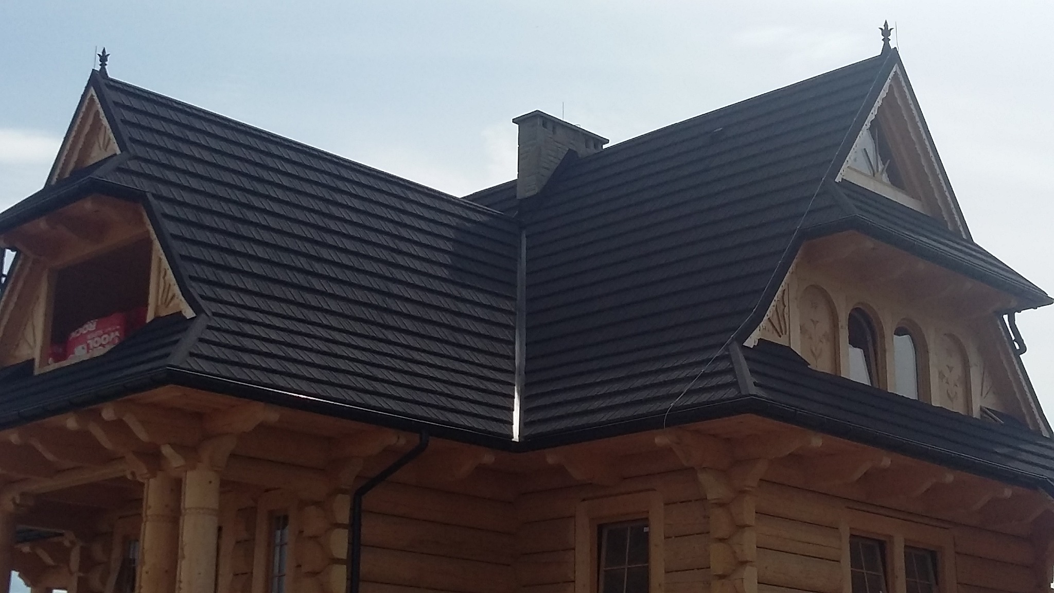 Dom w stylu zakopiańskim z ciemnym dachem, widoczny komin i ozdobne wykończenia okien dachowych.