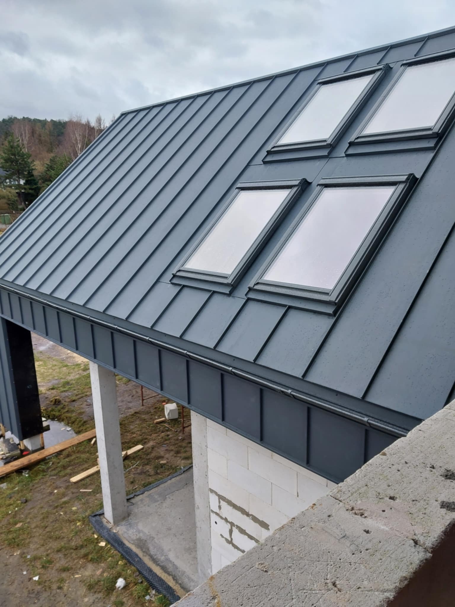 Szary dach z czterema oknami dachowymi w Leśnicy, widoczny z góry, z elementami konstrukcji w stanie surowym.