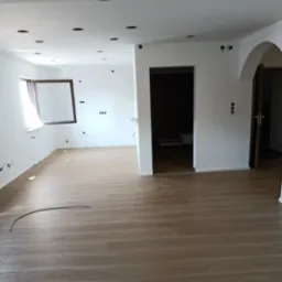 Jasne panele podłogowe w przestronnym wnętrzu z białymi ścianami, przygotowanym do montażu oświetlenia sufitowego i wykończenia instalacji elektrycznej.