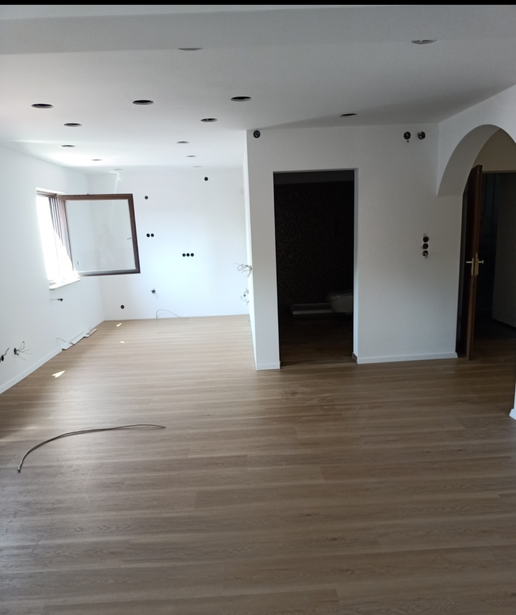 Jasne panele podłogowe w przestronnym wnętrzu z białymi ścianami, przygotowanym do montażu oświetlenia sufitowego i wykończenia instalacji elektrycznej.