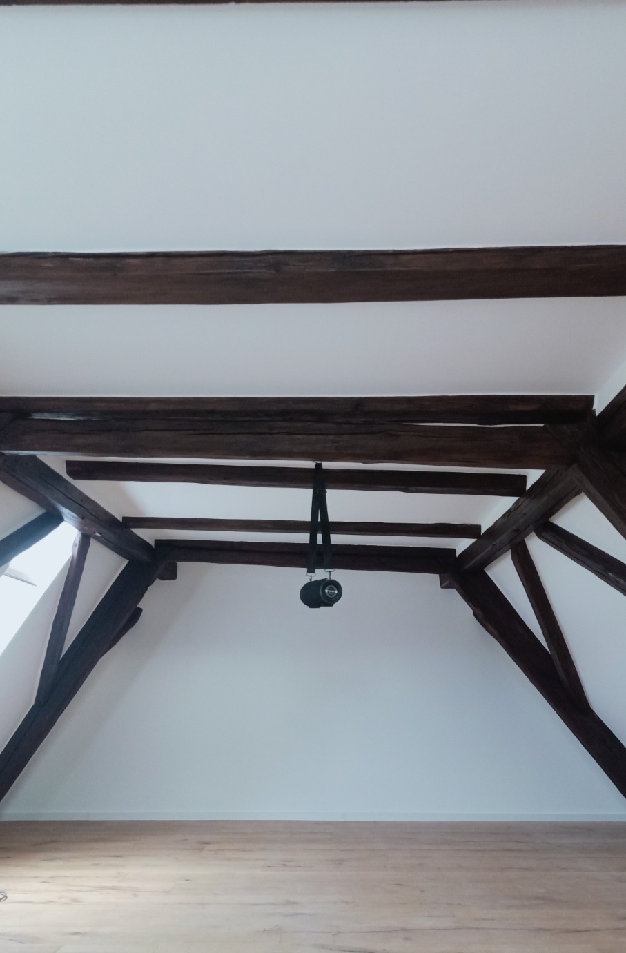 Poddasze z drewnianą konstrukcją dachu, świeżo po malowaniu na biało, z widocznym głośnikiem przenośnym wiszącym na belce.