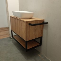 Marcin Konkol - Nowoczesna szafka łazienkowa z blatem z imitacji drewna i czarną metalową ramą, na której stoi biała umywalka nablatowa o kwadratowym kształcie.